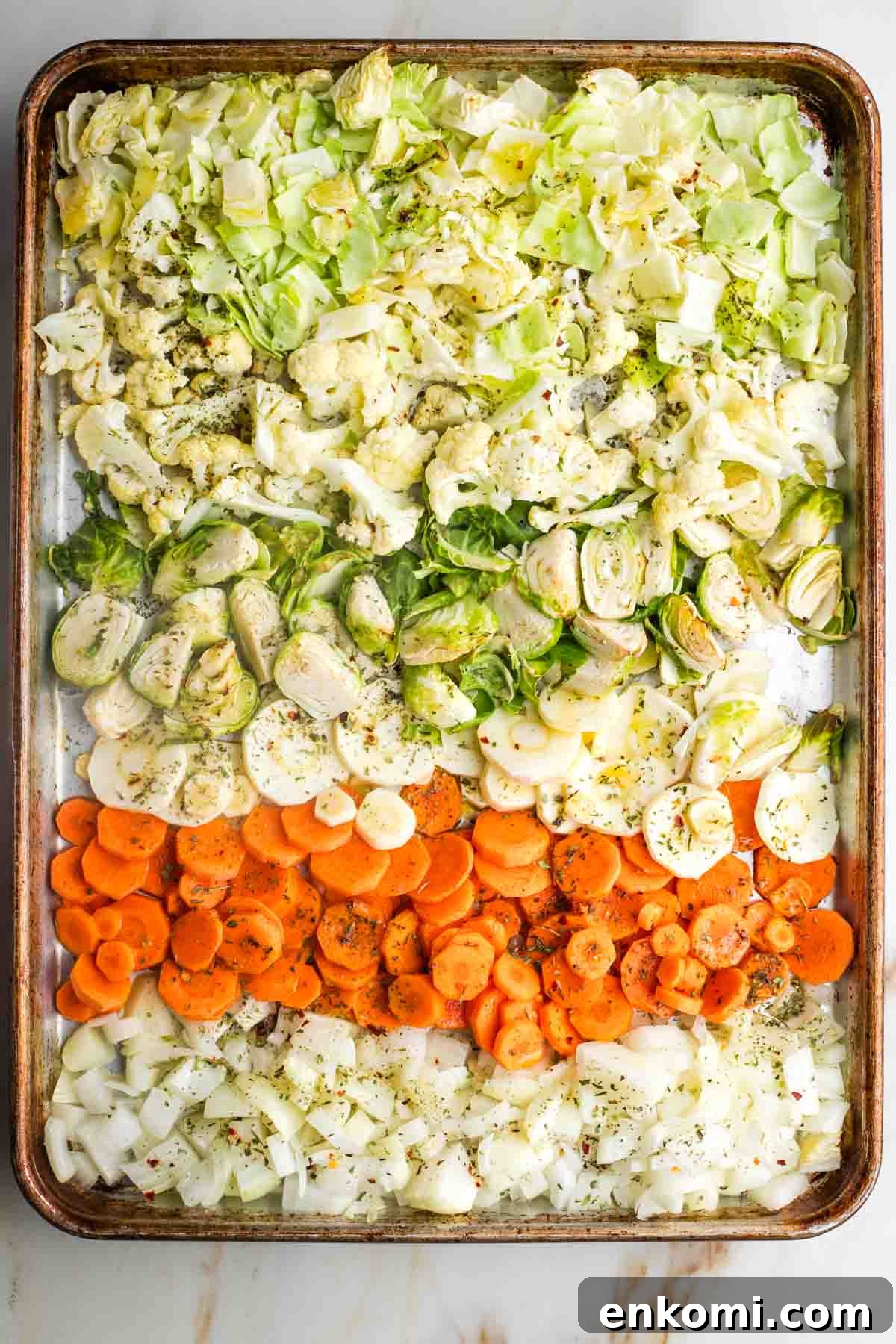Rows of chopped vegetables on a large baking tray, drizzled with oil and sprinkled with spices.