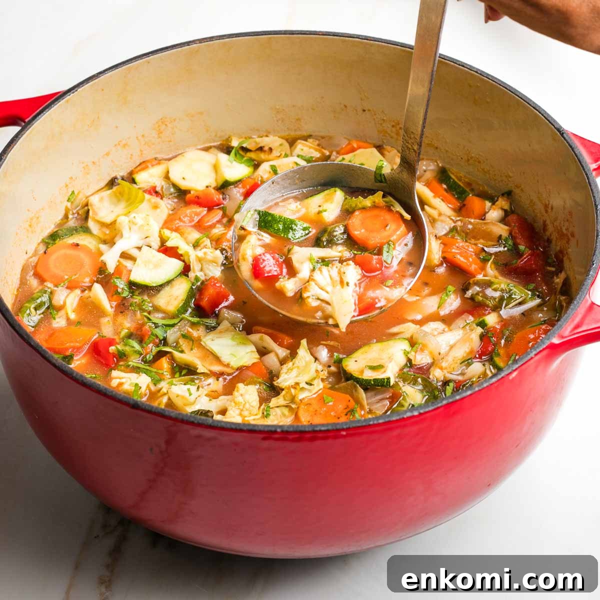 Chunks of roasted vegetables in a rich broth being ladled into bowls.