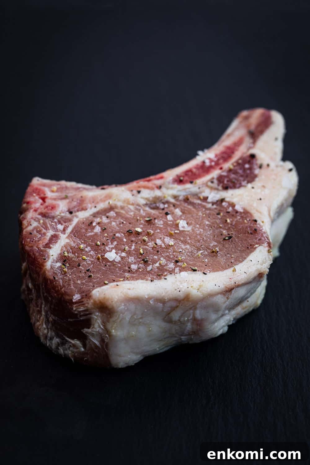 Up close shot of a raw seasoned pork chop; thick cut with the bone-in.