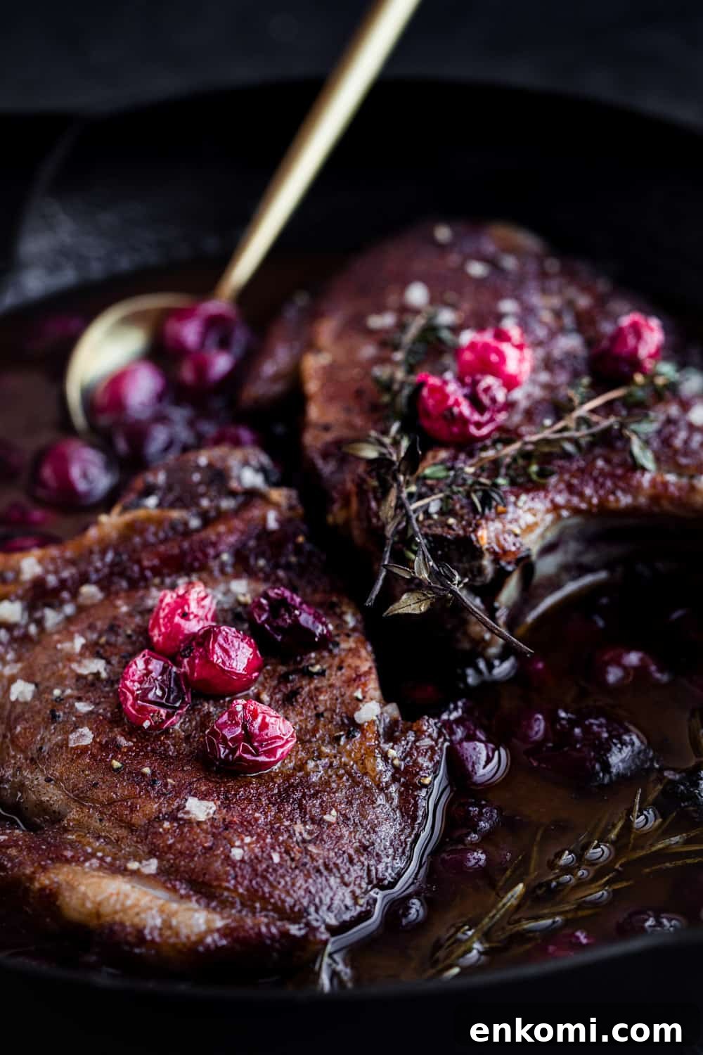 Post oven cranberry pork chop shot, chops in a cast iron skillet with a gold spoon and cranberry sauce, 45 degree angle uppitiest close shot.