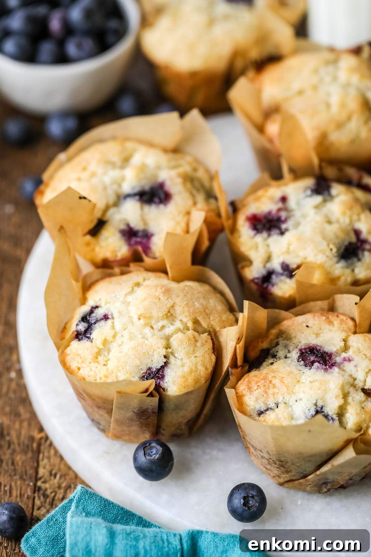 30 Muffin Recipes: Sweet, Savory & Seasonal Ideas 3 White plate of sourdough blueberry muffins in brown parchment wrappers.