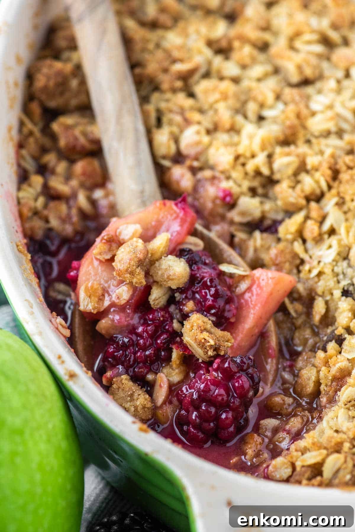 Apple and Blackberry Crumble Recipe for Summer Desserts 2 Wooden spoon dipped in baking dish of apple blackberry crumble.