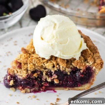Ice cream topped on cherry crumble pie on plate.