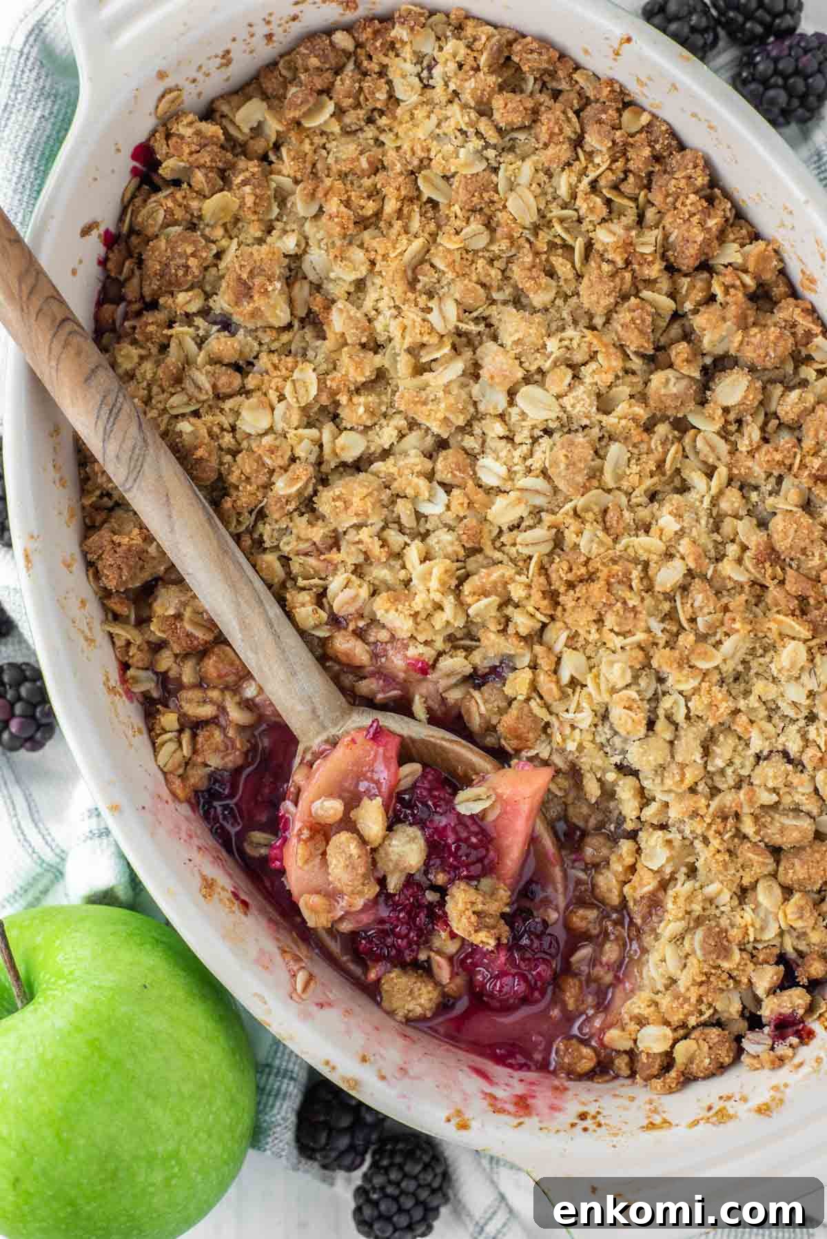 Apple and Blackberry Crumble Recipe for Summer Desserts 10 Oval baking dish of apple blackberry crumble with wooden spoon dipped into it.